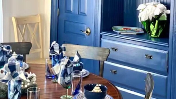 Een eetruimte met een blauwe deur, een kroonluchter en een tafel gedekt met servies en een schaal dessert.