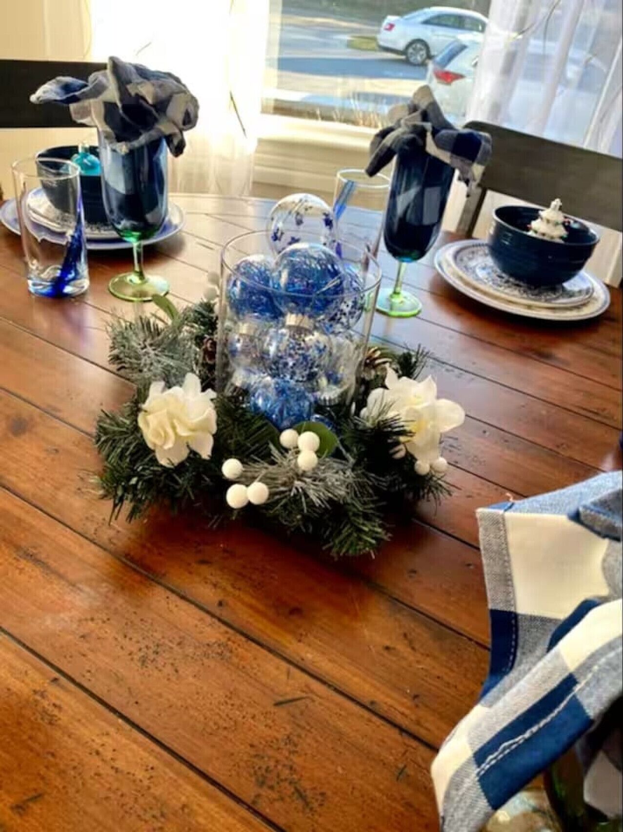 A dining table with a centerpiece of blue ornaments, white flowers, and greenery.