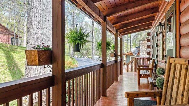 A wooden porch with a railing, potted plants, and a bench.