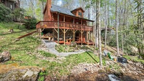 A rustic cabin with a wooden deck, surrounded by a forested area.