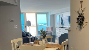 Zona pranzo con tavolo rotondo, sedie bianche e vista sull'oceano attraverso ampie finestre.