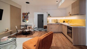 Una cocina moderna con armarios de madera, encimera negra y salpicadero amarillo. Hay una zona de comedor con una mesa redonda y sillas, y una sala de estar con sofá y mesa de centro.