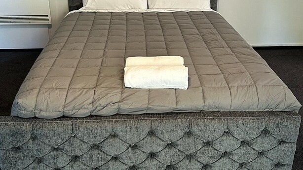 A bed with a tufted headboard, two pillows, and a folded blanket. - 301 Bealey Ave Motel (Christchurch)