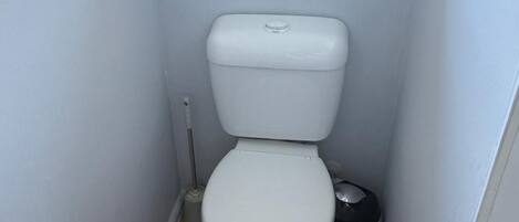 A compact bathroom with a white toilet, a bidet, and a small trash bin.