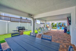 Eine Terrasse im Freien mit Grill, Esstisch und Stühlen, mit Blick auf einen Pool und einen umzäunten Garten.