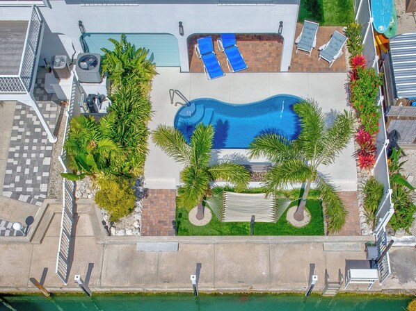 Luftaufnahme eines Poolbereichs mit kleinem Schwimmbecken, Liegestühlen und Palmen.