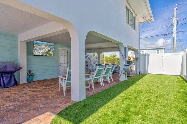A covered patio with outdoor seating, a grill, and a view of the neighborhood.