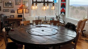 A rustic dining area with a round wooden table, chairs, a chandelier, and artwork on the walls. - Maison de LaMontagne: Unique hill top home with stunning views in Corinth (Corinth)