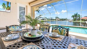 A dining area with a view of a pool and palm trees, featuring a table set with plates, glasses, and a potted plant.