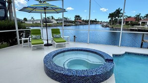 A pool area with a hot tub, lounge chairs, and a view of a marina.