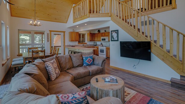 A spacious living room with a large sectional sofa, a wooden staircase, and a kitchen area. - Home with a Mountain View above the Angel Fire Golf Course (Angel Fire)