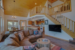 A spacious living room with a large sectional sofa, a wooden staircase, and a kitchen area. - Home with a Mountain View above the Angel Fire Golf Course (Angel Fire)