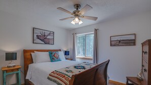 A bedroom with a wooden bed, a ceiling fan, a window with curtains, and two wall-mounted paintings. - Home with a Mountain View above the Angel Fire Golf Course (Angel Fire)