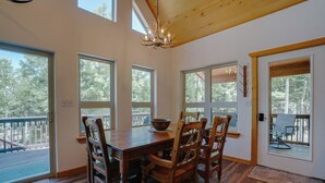 A dining area with a wooden table and chairs, large windows, and a chandelier. - Home with a Mountain View above the Angel Fire Golf Course (Angel Fire)