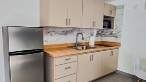 A compact kitchen with a stainless steel refrigerator, beige cabinets, a marble backsplash, and a tiled floor. - Private Colonial w/ Modern twist 2 BR w/Pkng & Laundry (Carolina)