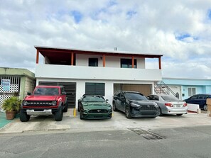 A two-story building with a garage parking several vehicles, including a red SUV and a green sports car.