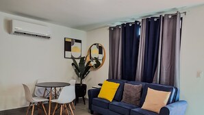 A living room with a blue sofa, a dining table with chairs, and a potted plant. - Private Colonial w/ Modern twist 2 BR w/Pkng & Laundry (Carolina)