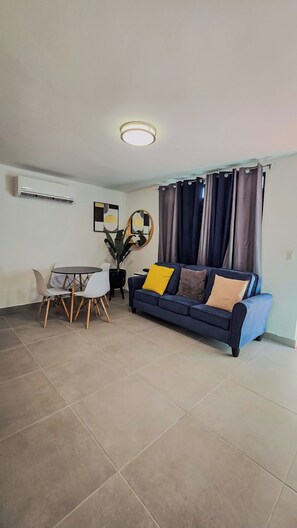 A living room with a sofa, a dining table with chairs, a potted plant, and a ceiling light. - Colonial Apartment w/ Parking & Patio, Near Beach (Carolina)