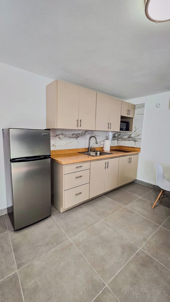 A modern kitchen with a stainless steel refrigerator, beige cabinets, a marble backsplash, and a white chair.