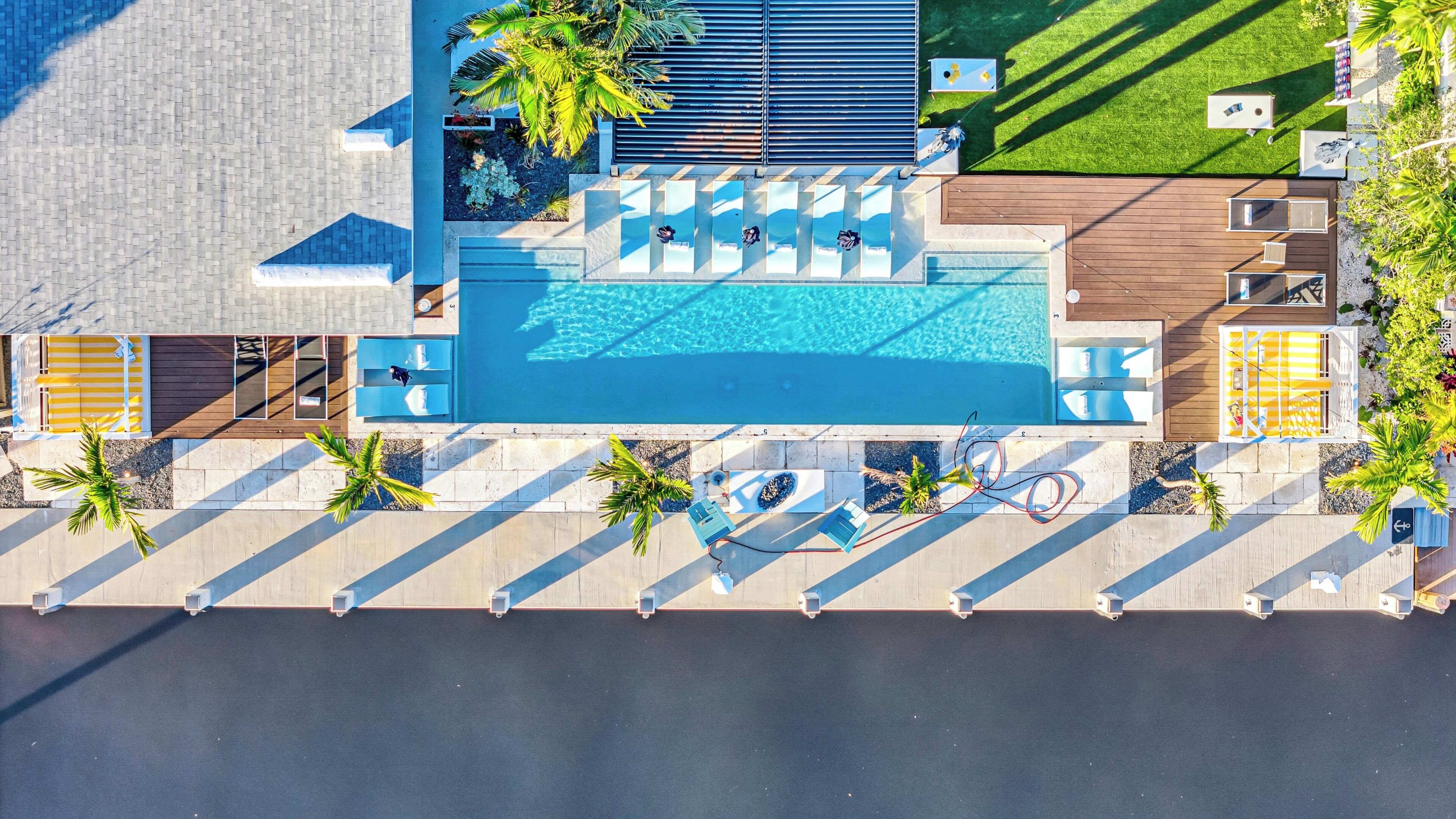 Eine Vogelperspektive auf ein modernes Resort mit einem zentralen Schwimmbecken, Liegestühlen und einem gepflegten Rasen.