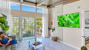 Un salón amplio con una televisión grande, un sofá, una mesa de centro y un ventanal corredero que da a un balcón.