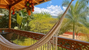 Una hamaca bajo una pérgola de madera con vistas a un jardín exuberante y montañas distantes.