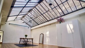 Una habitación amplia con techo alto, un tragaluz, una mesa de comedor con sillas, un armario blanco y un espejo.