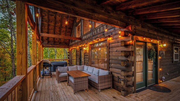 Una cabaña de troncos con una terraza de madera, un sofá y una mesa.