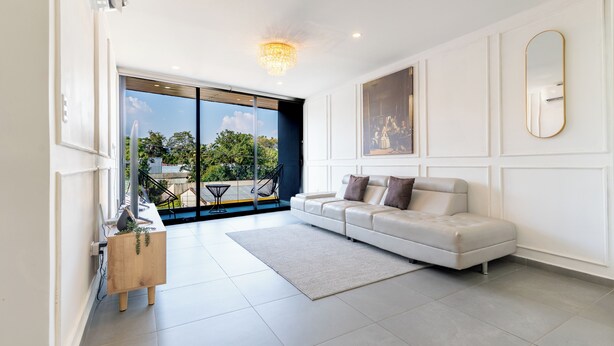 Ein modernes Wohnzimmer mit einem weißen Sofa, einem Kronleuchter und einem großen Fenster mit Blick ins Freie.