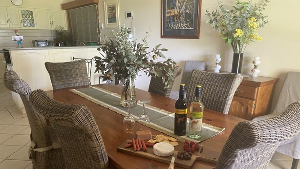 A dining area with a wooden table, wicker chairs, a vase with flowers, and a bottle of wine. - Private mooring with access to the main river, just 75 metres away. (Renmark)