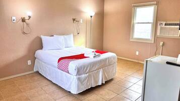 A bedroom with a bed, a desk, a lamp, and a window.