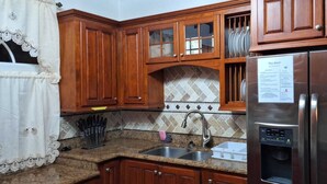 Cocina con armarios de madera, refrigerador de acero inoxidable, un lavamanos y salpicadero de azulejos.