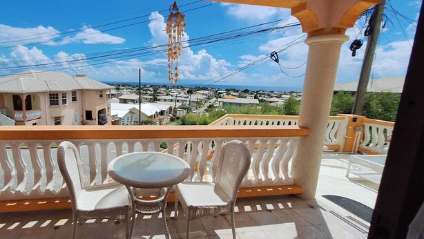 Un balcón con una mesa y sillas, con vista a una zona residencial con casas y cielo despejado.