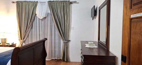Ein Hotelzimmer mit Bett, Nachttisch, Kommode, Spiegel und einem Fenster mit Vorhängen.