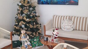 A living room with a Christmas tree, a painting, and a sofa with a 'Greetings' pillow.