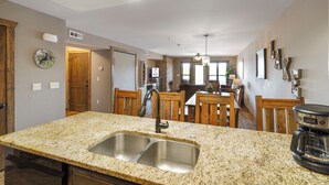 A kitchen with granite countertops, stainless steel sink, wooden chairs, and a dining table.