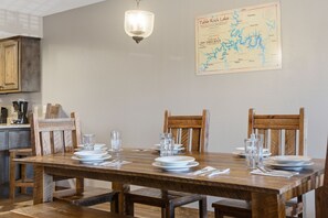 Un coin repas avec une table en bois dressée pour quatre personnes, des chaises, une carte accrochée au mur et un luminaire suspendu.