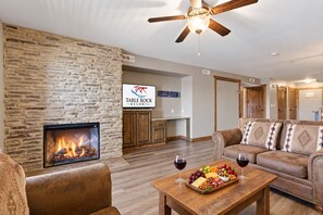 Un salon avec un mur en pierre, une cheminée, un ventilateur de plafond, une enseigne indiquant « Table Rock Resorts », et un coin salon avec une table dressée pour un repas.