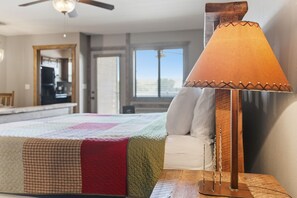 Une chambre à coucher avec un lit, une table de chevet, une lampe, un ventilateur de plafond et une vue sur l’extérieur.