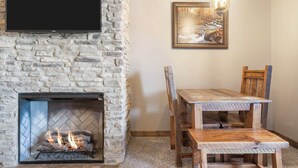 Una chimenea de piedra con un televisor montado encima, una mesa de comedor de madera con sillas, y un cuadro en la pared.