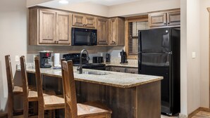 A kitchen with wooden cabinets, a black refrigerator, a microwave, a coffee maker, and a sink. - 1 Bed, sleeps 6, Lake Access, Swim, Fish, Kayak (Branson)