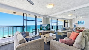 A spacious living area with a large TV, comfortable seating, and a balcony with a view of the ocean.