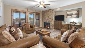 A spacious living room with a stone fireplace, leather sofas, and a ceiling fan. - 1 BD Lake Condo, Discount Tickets, Resort Perks and Free use of Kayaks (Branson)
