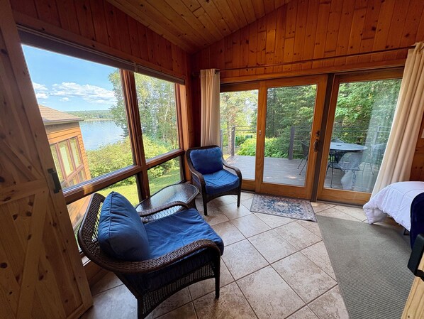 A wooden-paneled room with two wicker chairs and a view of a lake.