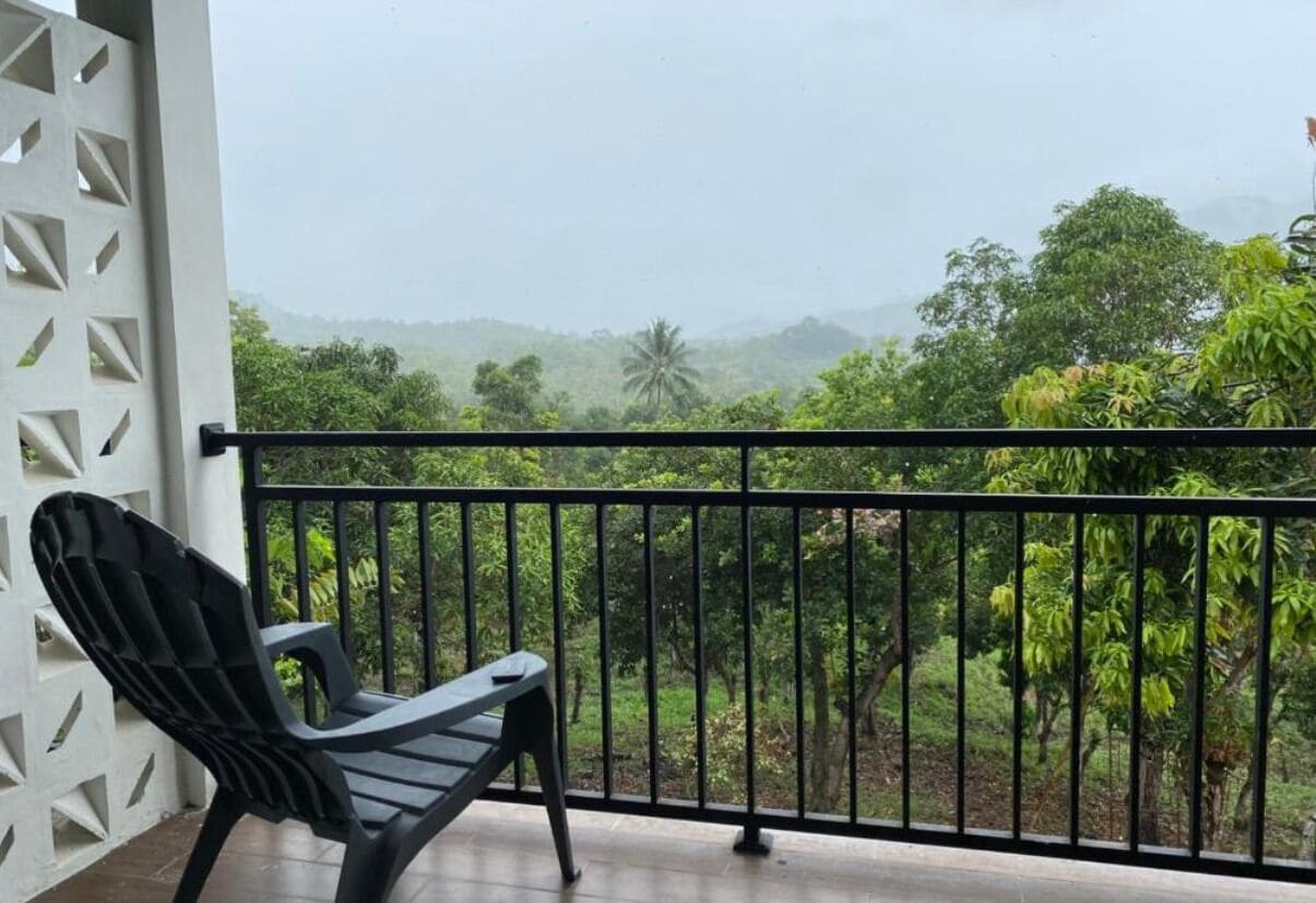 A balcony with a black chair, white lattice partition, and a view of lush greenery and hills.