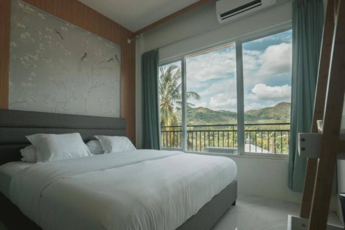 A bedroom with a large bed, a view of palm trees and hills, and a balcony with a railing.