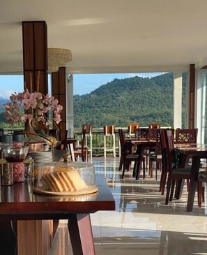 A dining area with tables and chairs, a buffet setup, and a view of a mountain. - Hakata Lejja near Natural Hot spring (Marioriawa)