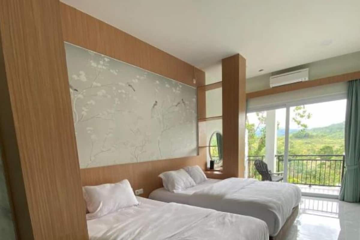 A hotel room with two beds, a large abstract painting on the wall, and a balcony with a view of greenery.
