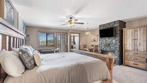 A bedroom with a bed, a wooden bench, a stone fireplace, and a TV mounted on the wall. - 1 Bedroom Lake Condo, sleeps 3, Resort Perks, Ticket/Golf Deals (Branson)