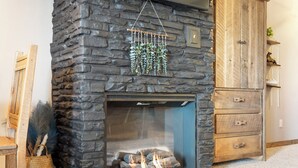 A stone fireplace with a hanging plant, a wooden cabinet, and a basket of feathers. - 1 Bedroom Lake Condo, sleeps 3, Resort Perks, Ticket/Golf Deals (Branson)
